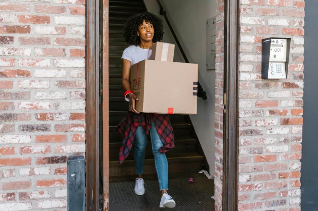 A woman is carrying carton outside her old apartment in the concept of moving to West London.