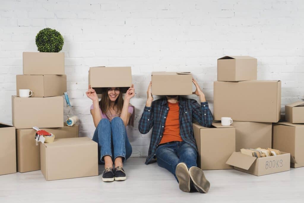 A young couple hiding their faces with moving carton in the concept of 'What Are the Hidden Costs in Home Removals Services'.